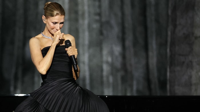 Céline Dion, vêtue d'une robe noire, est émue sur scène.