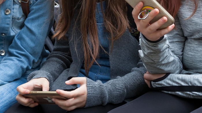 Des jeunes concentrés sur le contenu de leur cellulaire.