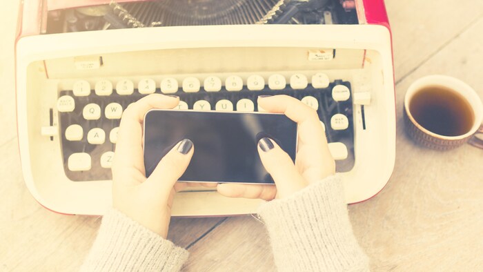 Des mains féminines tiennent un cellulaire au-dessus d'une vieille machine à écrire