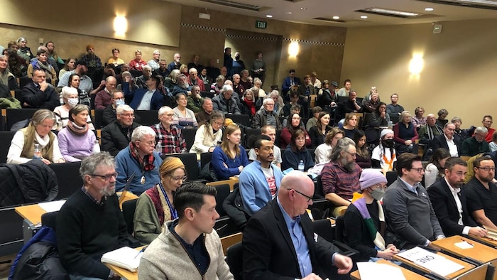 Une centaine de personnes assises sur des banquettes dans un auditorium à gradins.