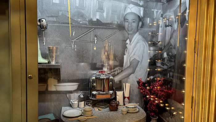 Une photo en noir et blanc d'un homme d'origine asiatique derrière une table d'une autre époque, avec des couverts.