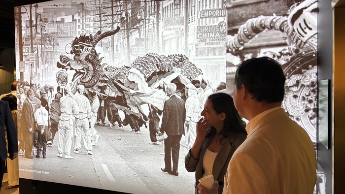 Des gens sont debout en train de parler devant une immense image en noir et blanc d'une danse traditionnelle du dragon.