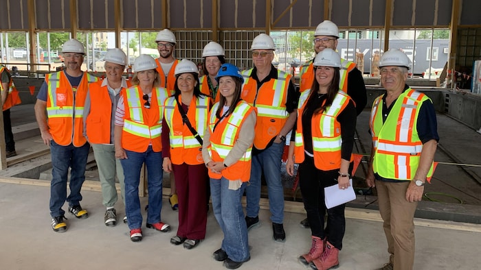Une dizaine de personnes, portant toutes une veste et un casque de sécurité, prennent la pose dans un bâtiment en chantier.