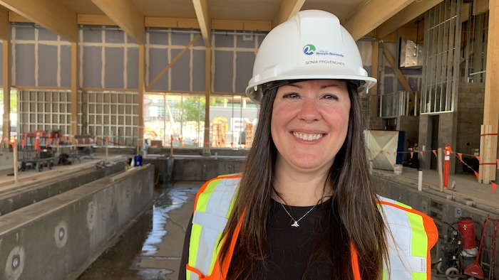 Sonia Provencher, casque de sécurité sur la tête, sourit à belles dents à la caméra devant une piscine en construction.