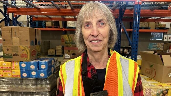 Une femme sourit à la caméra, devant des tablettes de produits.