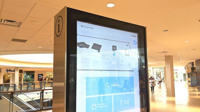 Vue sur l'intérieur d'un centre commercial. On voit un panneau interactif qui permet aux visiteurs de se retrouver dans l'immeuble.