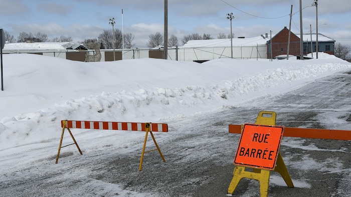 Un écriteau indiquant «rue barrée» et des petites barrières bloquant une rue enneigée.