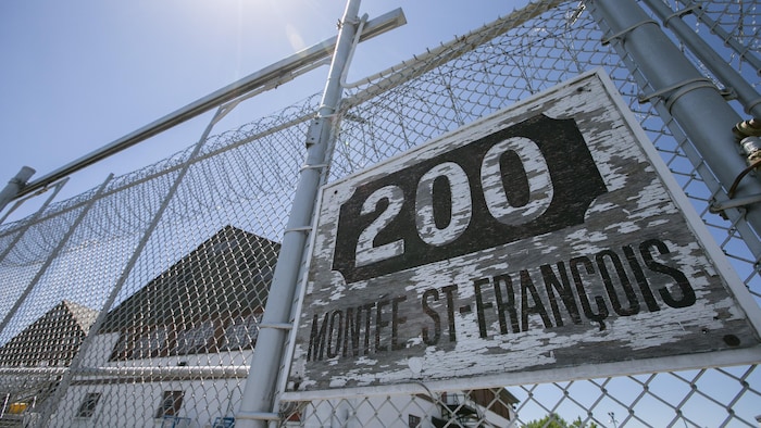 Une clôture à mailles losangées coiffée de barbelés, portant l'adresse « 200, montée Saint-François ».