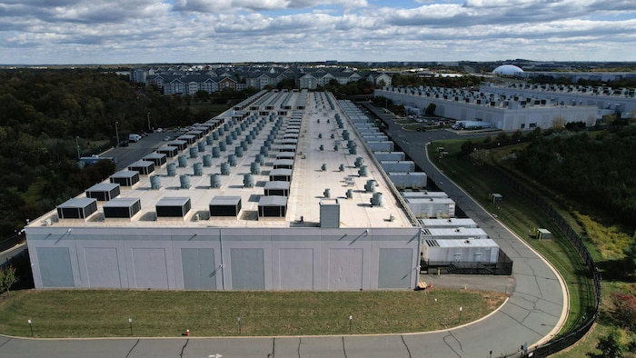 Photo aérienne de larges bâtiments rectangulaires blancs, hauts de seulement quelques mètres, avec de petits stationnements presque inoccupés.