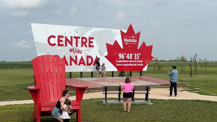 Une famille prend des photos devant le pancarte au parc du Centre du Canada.