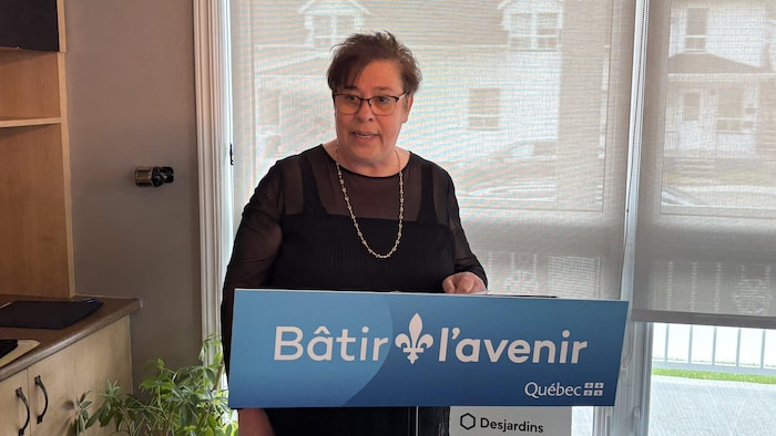 Une femme parle, debout derrière un lutrin portant une affiche du gouvernement du Québec.