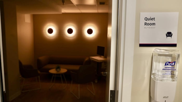 Un écriteau indiquant «Quiet Room» est posé à côté d'une porte qui s'ouvre pour laisser entrevoir une pièce sombre aux lueurs brunâtres et jaunes.