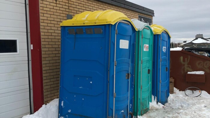 Trois toilettes chimiques à l'extérieur d'un bâtiment.