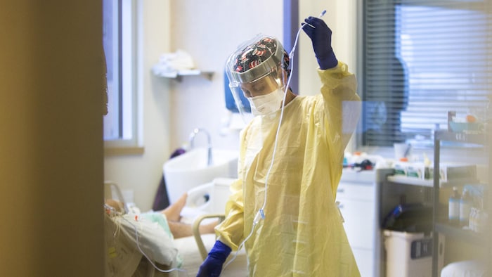 Une infirmière revêtue d'un équipement de protection individuelle est en plein travail auprès d'un patient atteint de COVID-19.