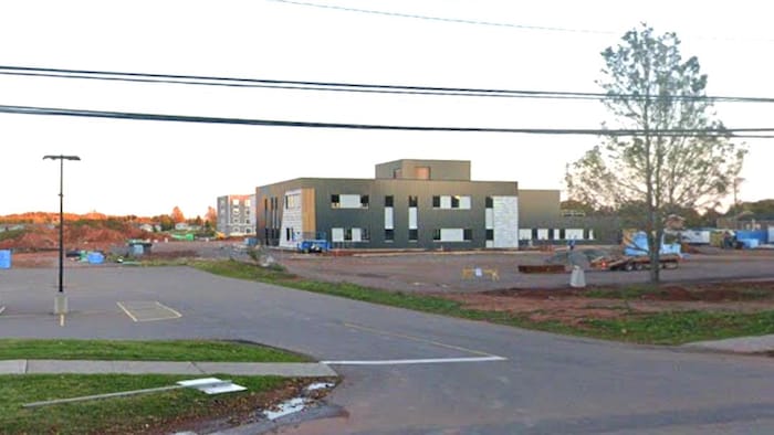 Un bâtiment gris d'apparence neuve, sur un terrain qui n'a pas encore été asphalté, entouré de machinerie.