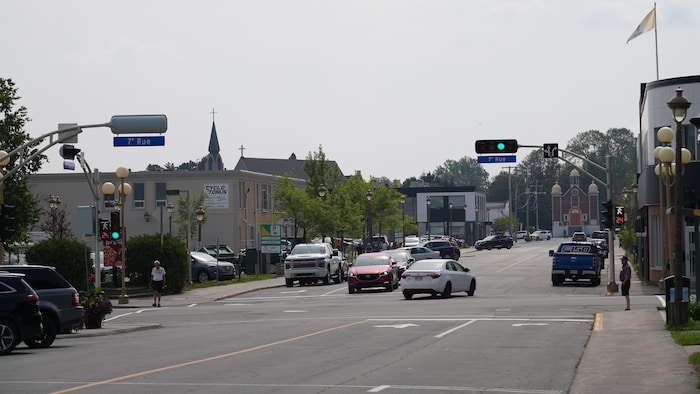 Des véhicules circulant sur la 2e Avenue à Val-d'Or, un passant qui traverse une intersection et un autre passant qui attend pour traverser à un autre coin de rue.