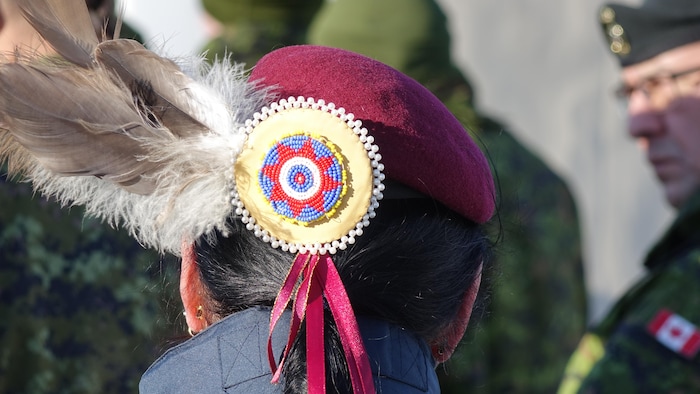 Une femme de dos, avec une broche traditionnelle dans les cheveux et des plumes. 