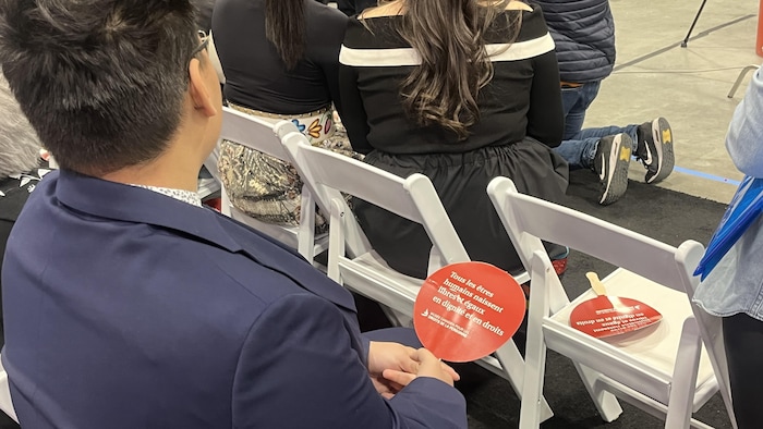 Une personne tient un pamphlet sur lequel on lit un message portant sur l'égalité des personnes, le 18 mai 2025 à Winnipeg
