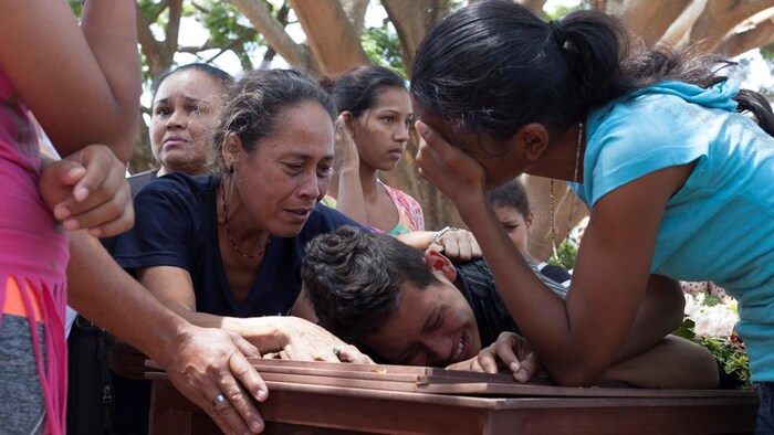 Des gens pleurent, appuyés sur le cercueil d'Abraham Duran, l'un des prisonniers qui est mort lors de l'émeute d'une prison au Venezuela. 