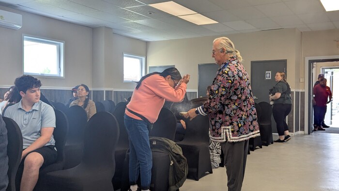 Une cérémonie traditionnelle autochtone se déroule dans une salle en présence de plusieurs personnes.
