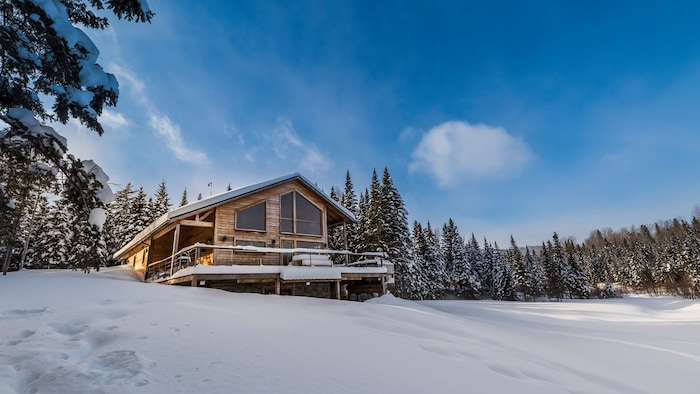 Chalet en bois perché au sommet d'une colline enneigée entourée de conifères dans Charlevoix.