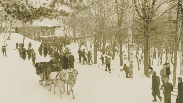 Une foule fait du ski au sommet du mont Royal, non loin du chalet. On y voit une calèche avec des chevaux.