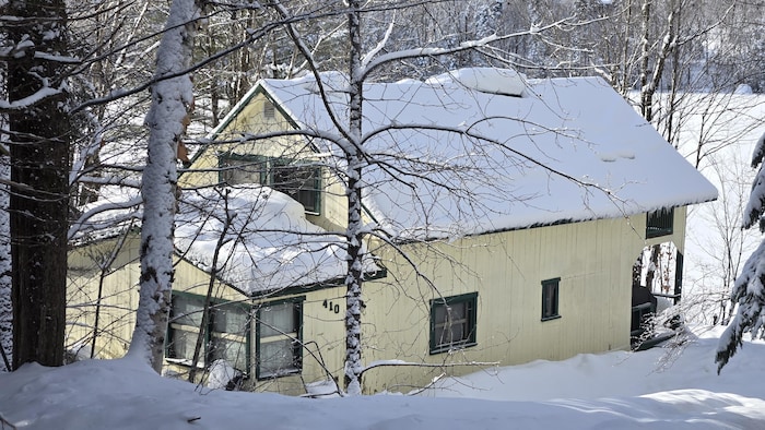 Un chalet situé sur le bord d’un lac, dans un milieu boisé, en hiver.
