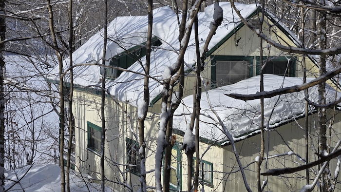 Un chalet situé sur le bord d’un lac, dans un milieu boisé, en hiver.