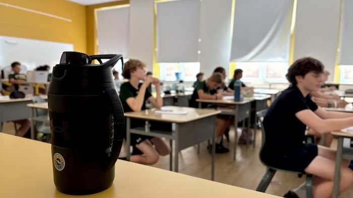 Des élèves dans une classe, en gros plan, une gourde d'eau.
