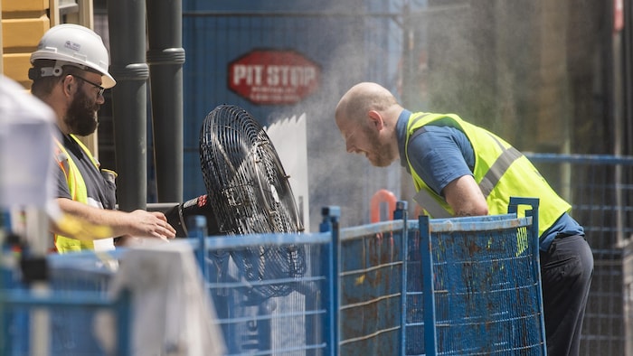 Un travailleur utilise un ventilateur brumisateur pour se rafraîchir. 