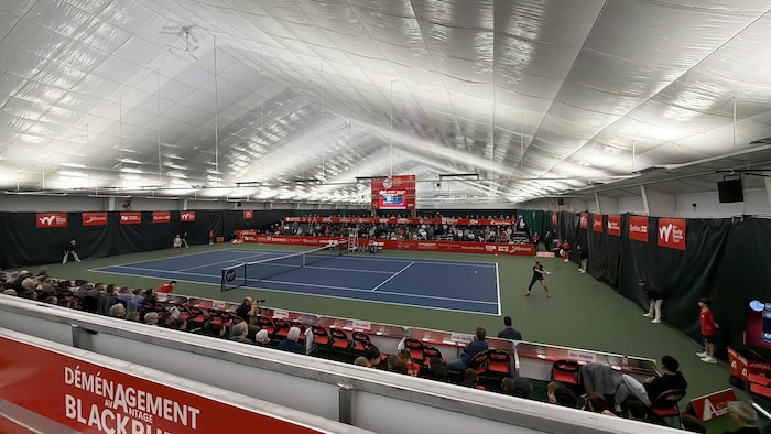 Deux joueuses disputent un match de tennis sur un court intérieur sous un grand dôme blanc.