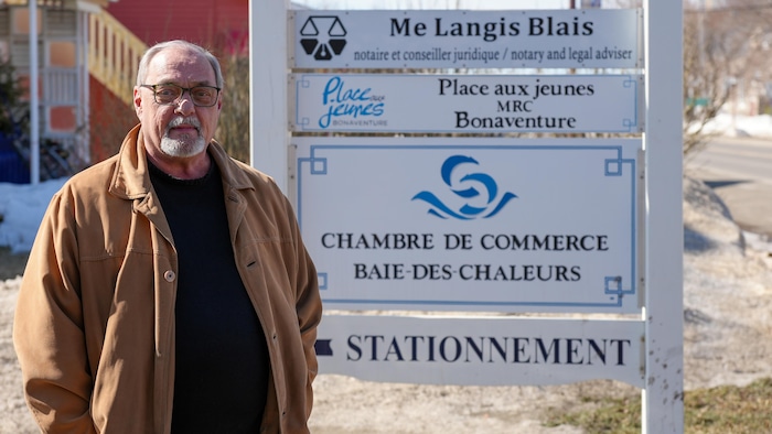 Le directeur général de la Chambre de commerce Baie-des-Chaleurs, Maurice Quesnel, devant une affiche.