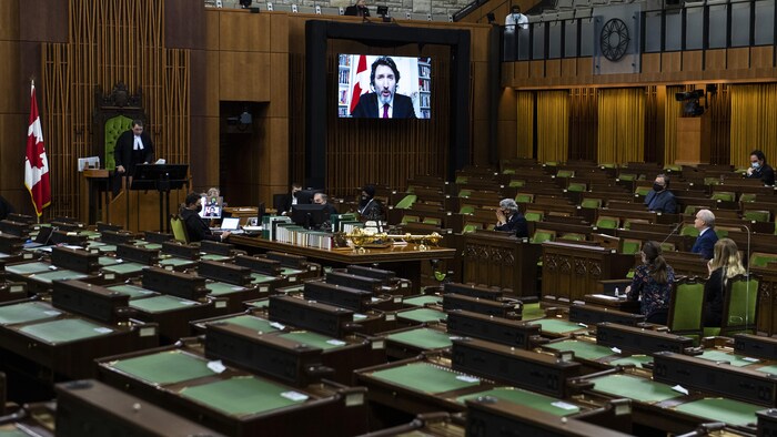 Quelques députés regardent un écran où apparaît Justin Trudeau.
