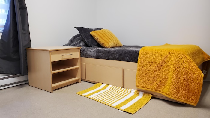 Une petite chambre à coucher avec un lit à une place et des couvertures grises et jaunes installées dessus.
