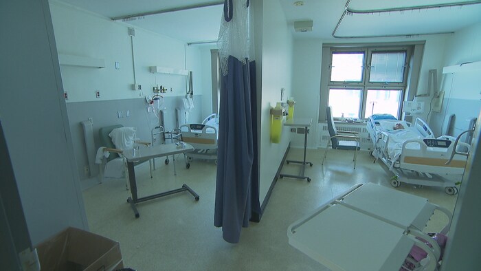 Un homme est couché dans un lit d'hôpital. L'autre lit est vide.