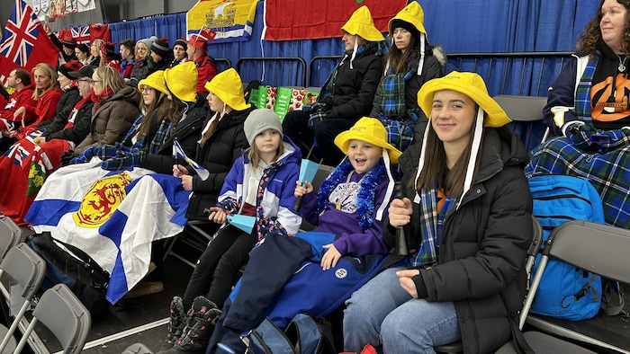 Des personnes, notamment des adultes, sont assises sur des chaises, dont certaines ont des drapeaux sur les cuisses et derrière, le 22 février 2025 à Saskatoon. 