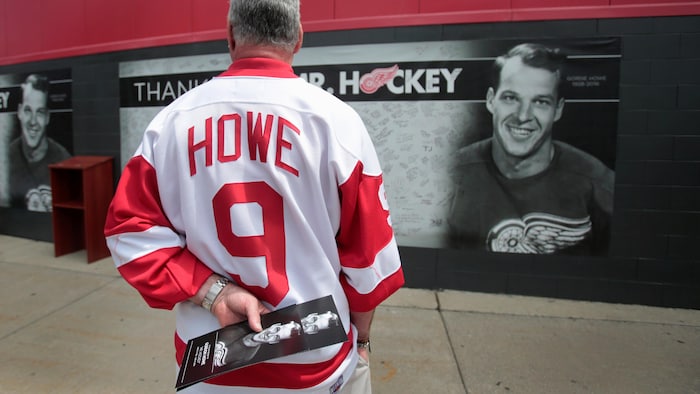 Un homme avec un chandail de Gordie Howe se tient devant un panneau commémoratif du joueur de hockey.