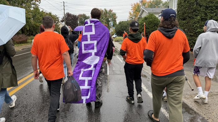 Des jeunes portant un chandail orange marchent le long d'une route.