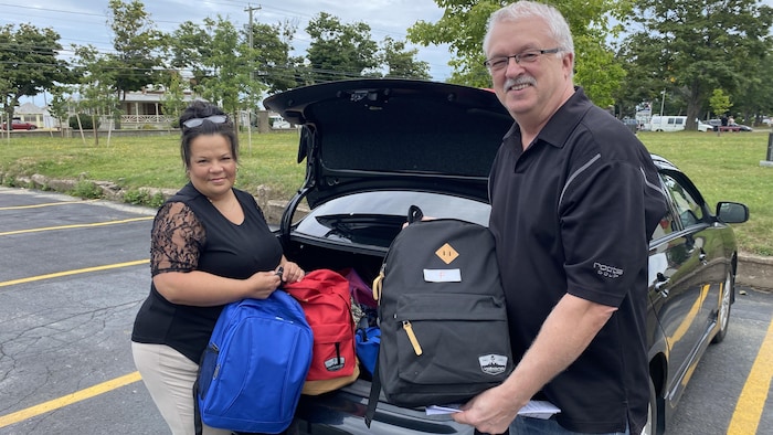 Chantal Richardson et René Pinet montrent des sacs d'école qu'ils s'apprêtent à charger dans le coffre d'une voiture. 