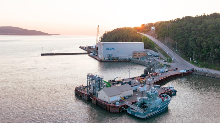 Un remorqueur est amarré à un quai sur une photo aérienne d'un chantier maritime au coucher du soleil.