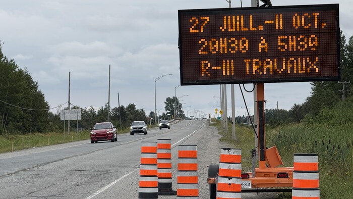 Un panneau électronique bordé de cônes en bordure de route indique les dates et les heures d'entraves.