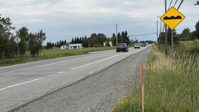 Des voitures circulent sur une route où l'on voit un panneau indiquant une chaussée cahoteuse.