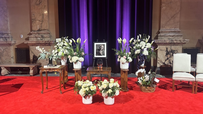 La photo et l'urne d'Oliver Jones exposées en chapelle ardente, entourées d'arrangements floraux.