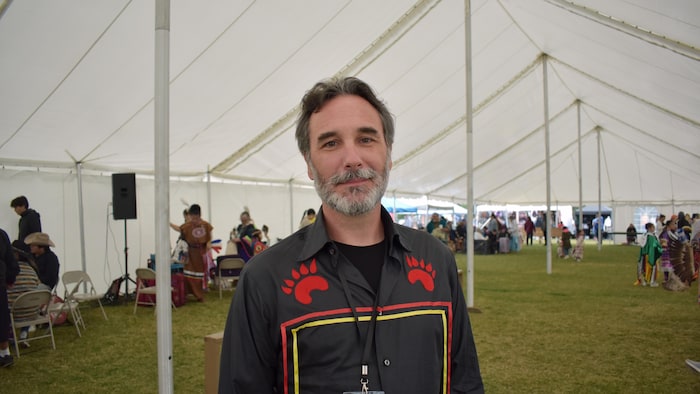 Portrait d'un homme portant une chemise ornée d'empreintes d'ours rouges sous un grand chapiteau.