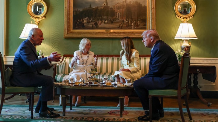Charles III, Camilla, Melania et Donald Trump assis dans un salon autour d'une table où sont posés du miel, du thé et des pâtisseries.