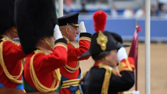 King Charles III in official red gives a military salute. 