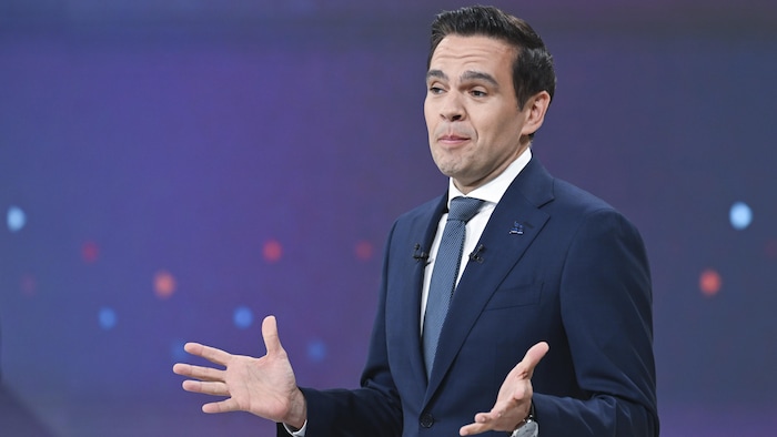 Charles Milliard s'exprime derrière son pupitre en faisant des gestes des mains.