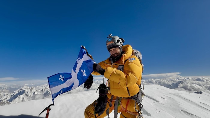 Un homme au sommet d'une montagne enneigée, tenant le drapeau québécois.