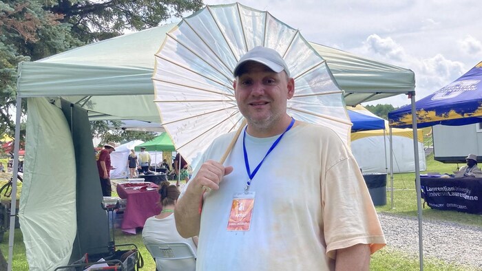 Charles Tossell tient un parasol devant des kiosques au festival.