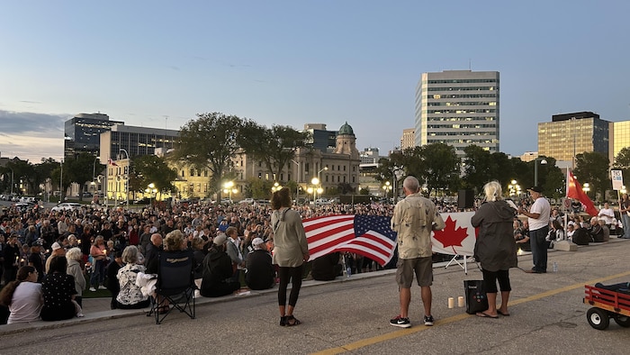Foule devant le Palais législatif. Les organisateurs y tiennent des drapeaux du Canada et des États-Unis. 